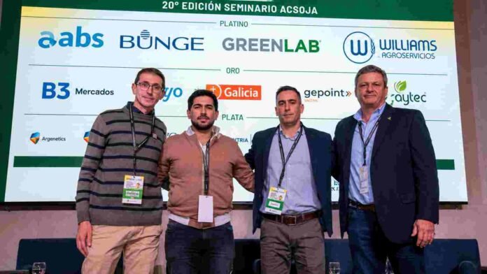 Cuatro participantes del Seminario ACSOJA posan frente al panel de sponsors durante el encuentro agroindustrial.