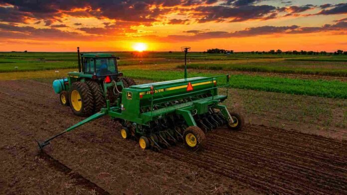 Tractor con sembradora trabajando en un lote agrícola argentino al atardecer, bajo un cielo de tonos anaranjados y dorados, con el sol sobre el horizonte y colores intensos que reflejan el inicio de una nueva campaña agrícola.