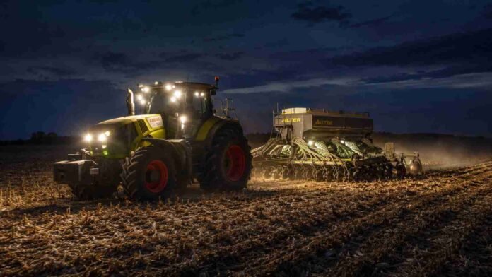 Tractor Claas con sembradora de Industrias Alter realizando la siembra de trigo de noche sobre un campo con rastrojo de maíz, con luces encendidas y cielo parcialmente nublado.