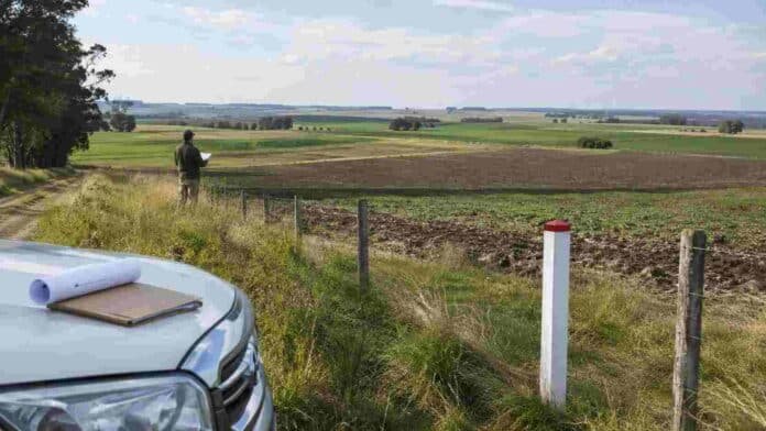 tierras-en-venta-ley-de-tierras-ruralnet Vista de campos productivos delimitados con alambrado y mojones, con un productor inspeccionando la tierra, en una imagen que ilustra la compraventa de tierras rurales en Argentina.