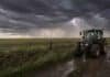 Se activa la inestabilidad: tormentas aisladas, ráfagas y heladas alcanzan al campo hasta el viernes Tractor Valtra en un camino rural húmedo bajo un cielo de tormenta, con pastizales movidos por el viento, cortinas de lluvia y un relámpago sobre el campo argentino.