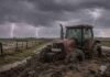 Pronóstico trimestral: dónde lloverá más y qué zonas tendrán temperaturas superiores Tractor Case empantanado y cubierto de barro en un camino rural de la pampa húmeda, junto a un alambrado, bajo una tormenta con lluvia intensa y relámpagos.