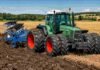 El tractor que revolucionó la transmisión agrícola cumple 30 años y Fendt lo celebra con solo 300 unidades especiales Tractor agrícola verde con arado trabajando sobre un lote cosechado, removiendo el suelo en un campo rural bajo cielo despejado.