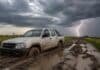 Prevén tormentas de hasta 80 mm en Santa Fe, Entre Ríos y Corrientes Camioneta pickup doble cabina encajada en un camino rural embarrado del Litoral argentino, con profundos surcos, charcos y un cielo de tormenta con relámpago al fondo.