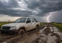 Prevén tormentas de hasta 80 mm en Santa Fe, Entre Ríos y Corrientes Camioneta pickup doble cabina encajada en un camino rural embarrado del Litoral argentino, con profundos surcos, charcos y un cielo de tormenta con relámpago al fondo.