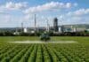 La suba de los fertilizantes le costó USD 180 millones extra al agro argentino Pulverizador agrícola realizando una aplicación sobre un cultivo, con un complejo industrial vinculado al agro en el fondo.