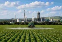 La suba de los fertilizantes le costó USD 180 millones extra al agro argentino Pulverizador agrícola realizando una aplicación sobre un cultivo, con un complejo industrial vinculado al agro en el fondo.