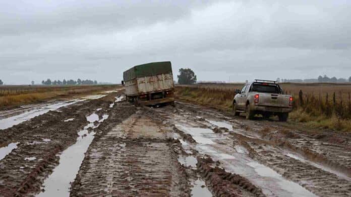 Camino rural de la provincia de Buenos Aires con barro y grandes huellas, mientras un camión y una camioneta avanzan con dificultad tras las lluvias.