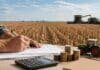 El agro recibe más crédito, pero en granos son apenas US$32 por tonelada Productor gestionando financiamiento frente a un campo en cosecha, con maquinaria agrícola y monedas como representación del crédito al agro.
