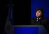 Milei defendió el rumbo económico y destacó el crecimiento Orador durante un discurso en un acto oficial, frente a un atril y con la bandera argentina de fondo.