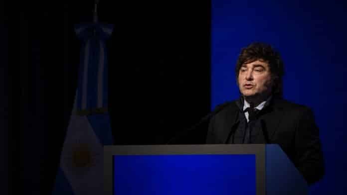 discurso-acto-oficial-argentina Orador durante un discurso en un acto oficial, frente a un atril y con la bandera argentina de fondo.
