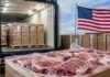 Por qué Argentina no accede a la nueva cuota de 300.000 toneladas de carne que abrió Trump Cajas de carne vacuna envasada para exportación frente a un contenedor de carga refrigerado, con una bandera de Estados Unidos al fondo.