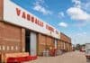 La planta de Vassalli intenta reactivarse en medio de reclamos salariales y un embargo Fachada de la fábrica Vassalli en Firmat, Santa Fe, con maquinaria y vehículos en el predio industrial bajo un cielo azul con nubes.