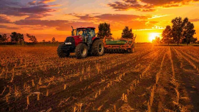 siembra-campo-atardecer-tractor-agosto-2026 Tractor con sembradora trabajando en un lote agrícola al atardecer, con cielo naranja y el sol sobre el horizonte.
