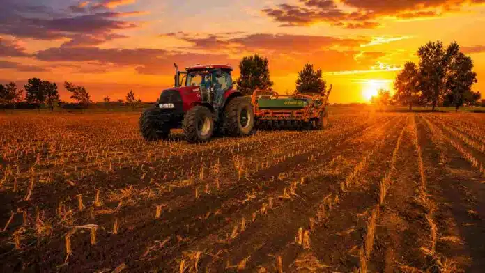 siembra-campo-atardecer-tractor-agosto-2026 Tractor con sembradora trabajando en un lote agrícola al atardecer, con cielo naranja y el sol sobre el horizonte.