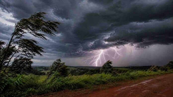 Tormenta eléctrica intensa sobre un paisaje rural, con relámpago potente, nubes oscuras, viento fuerte y camino de tierra en primer plano