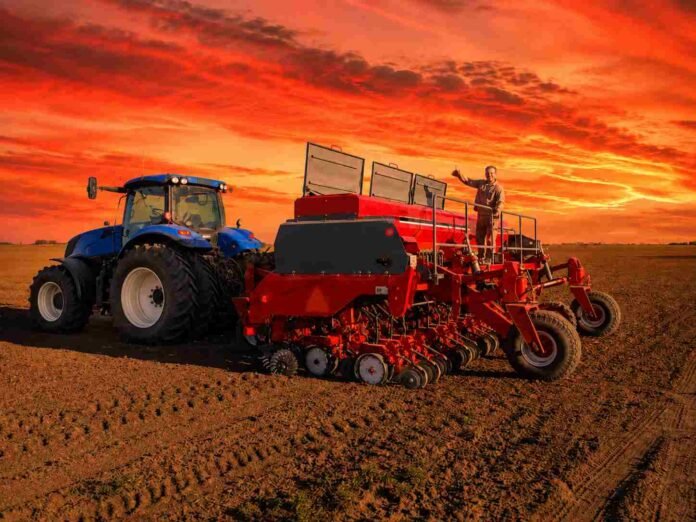 tractor-sembradora-atardecer-campo Tractor azul y sembradora roja trabajando en un campo agrícola durante un atardecer de tonos rojizos