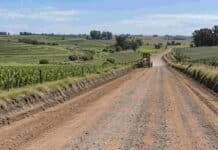 Córdoba fusiona por primera vez un consorcio caminero y uno de suelos en un esquema integral Camino rural en zona agrícola de Córdoba con una motoniveladora trabajando, rodeado de campos cultivados y obras de conservación del suelo.