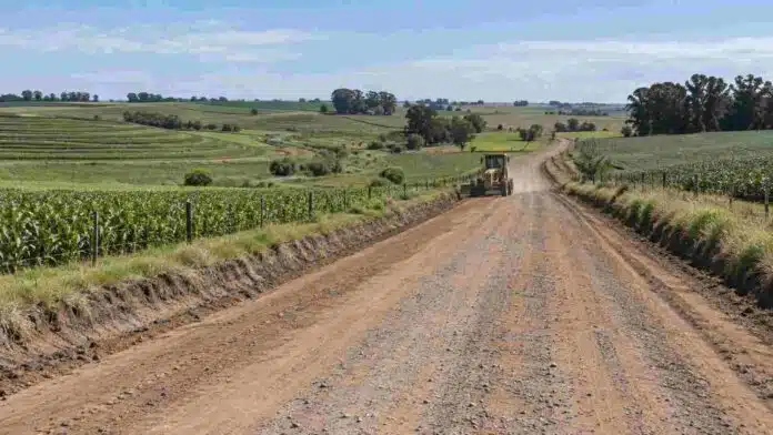 Camino rural en zona agrícola de Córdoba con una motoniveladora trabajando, rodeado de campos cultivados y obras de conservación del suelo.