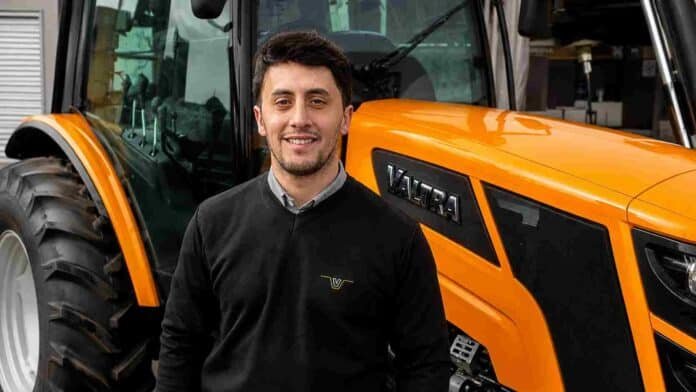 Ejecutivo de Valtra posa frente a un tractor naranja de la marca durante una exposición agropecuaria.