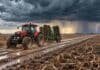 Pronóstico del 1 al 3 de octubre: el sábado suma más zonas con lluvias y tormentas Tractor con implemento agrícola avanza por un camino embarrado entre lotes en barbecho, bajo nubes de tormenta y un relámpago en el horizonte