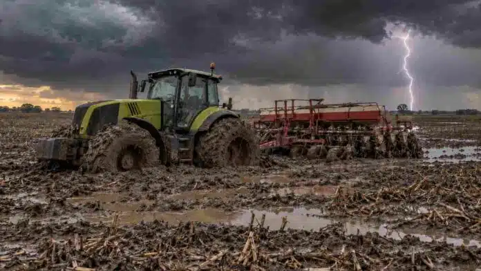 pronostico-lluvias-rafagas-14-provincias-ruralnet Tractor con sembradora encajado en un lote con rastrojo de maíz, barro y charcos durante una tormenta con relámpagos