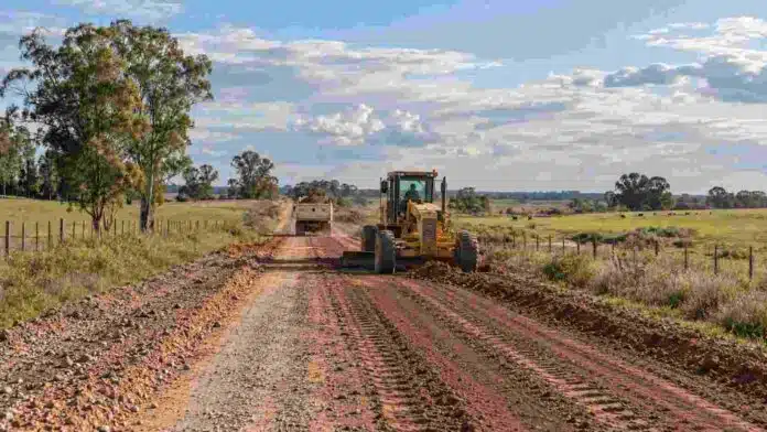 Motoniveladora trabaja en la reparación de un camino rural de Entre Ríos, junto a un camión con material para mejorar la traza.