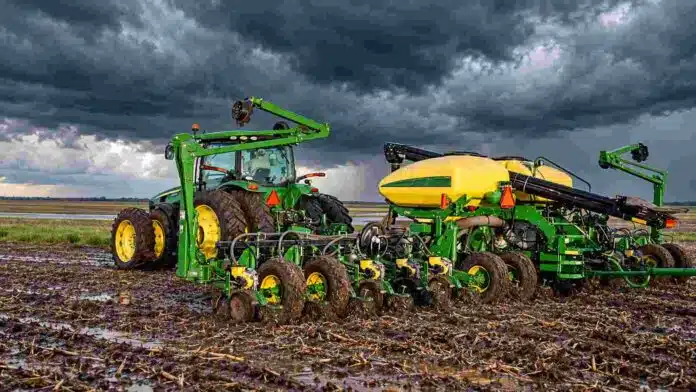 sembradora-john-deere-tormenta-ruralnet Tractor y sembradora John Deere trabajan sobre un lote con suelo húmedo bajo un cielo de tormenta con nubes oscuras.