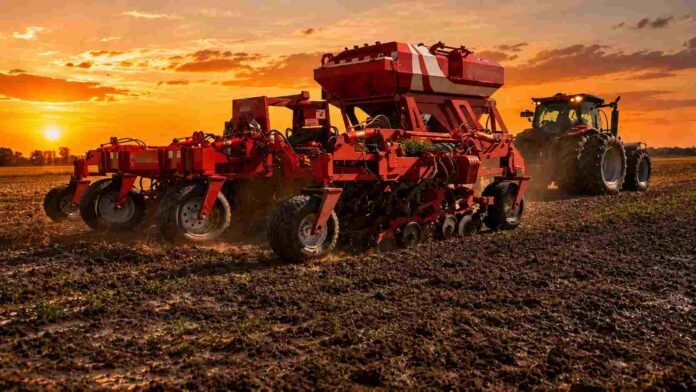Sembradora trabajando sobre suelo húmedo en un campo de la Pampa Húmeda durante un atardecer de cielo naranja.