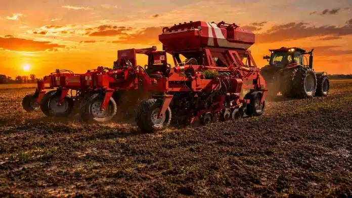Sembradora trabajando sobre suelo húmedo en un campo de la Pampa Húmeda durante un atardecer de cielo naranja.