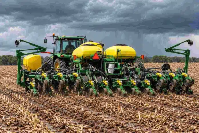 siembra-maiz-suelo-humedo-nubes-lluvia Tractor con sembradora de maíz trabajando sobre rastrojo y suelo húmedo bajo un cielo cubierto por nubes de lluvia.