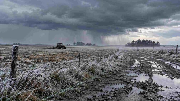 Tormenta sobre un campo rural con suelo húmedo, escarcha, camino embarrado y un tractor bajo un marcado descenso de temperatura.