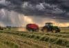 El tiempo cambia este fin de semana: tormentas fuertes, ráfagas y marcado descenso térmico Tractor con rotoenfardadora trabajando sobre alfalfa bajo una tormenta, con rollos en el campo y lluvias intensas en el horizonte.