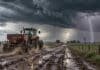Tormentas fuertes con granizo y hasta 70 mm: las zonas bajo alerta Tractor se aleja por un camino rural embarrado bajo una tormenta intensa, con lluvia, nubarrones oscuros y un relámpago en el horizonte.