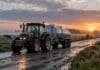 Récord lácteo: las exportaciones llegaron a 1.835 millones de litros Tractor remolcando un acoplado tanque de transporte de leche sobre un camino rural mojado al amanecer, con pasturas y vacas al fondo.