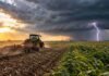 Pronóstico para viernes, sábado y domingo: la inestabilidad se extiende a 14 provincias Tractor trabajando en un campo rural bajo un cielo tormentoso, con un relámpago al fondo y cultivos verdes en primer plano.