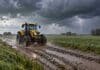 El SMN alerta por tormentas en el norte y lluvias intensas en Buenos Aires este martes Tractor Valtra amarillo avanza por un camino rural embarrado bajo la lluvia, con un relámpago sobre los campos al fondo