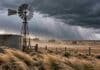 Ráfagas de 70 km/h, Zonda y nieve de 30 cm afectan a 13 provincias Viento fuerte sobre un campo argentino con molino y tanque australiano bajo cielo de tormenta