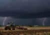 Alerta naranja por tormentas: hasta 100 mm en nueve provincias Tractor trabajando en un campo agrícola bajo un cielo cubierto de nubes negras de tormenta, con dos relámpagos y lluvias intensas en el horizonte.