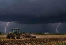 Alerta naranja por tormentas: hasta 100 mm en nueve provincias Tractor trabajando en un campo agrícola bajo un cielo cubierto de nubes negras de tormenta, con dos relámpagos y lluvias intensas en el horizonte.