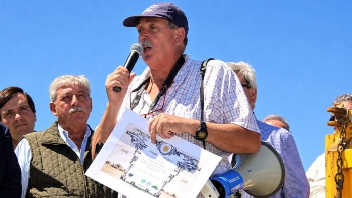 Armando Zabala habla con un micrófono durante un acto rural, acompañado por productores agropecuarios, mientras sostiene un reconocimiento.