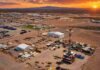 Vaca Muerta impulsa récords de petróleo y gas en Argentina Vista aérea de un campamento petrolero con equipo de perforación, instalaciones operativas y vehículos en una zona árida, bajo un cielo de atardecer con colores intensos.