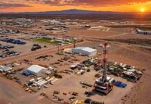 Vaca Muerta impulsa récords de petróleo y gas en Argentina Vista aérea de un campamento petrolero con equipo de perforación, instalaciones operativas y vehículos en una zona árida, bajo un cielo de atardecer con colores intensos.