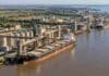 Agro argentino: un estudio revela que podría exportar US$ 122.000 millones si hubiera crecido como Brasil Vista aérea de una terminal agroexportadora con silos y buques cargueros sobre un río, ilustrando el comercio exterior agroindustrial argentino y su comparación con Brasil.