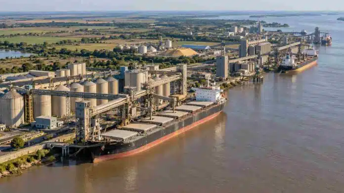 Vista aérea de una terminal agroexportadora con silos y buques cargueros sobre un río, ilustrando el comercio exterior agroindustrial argentino y su comparación con Brasil.