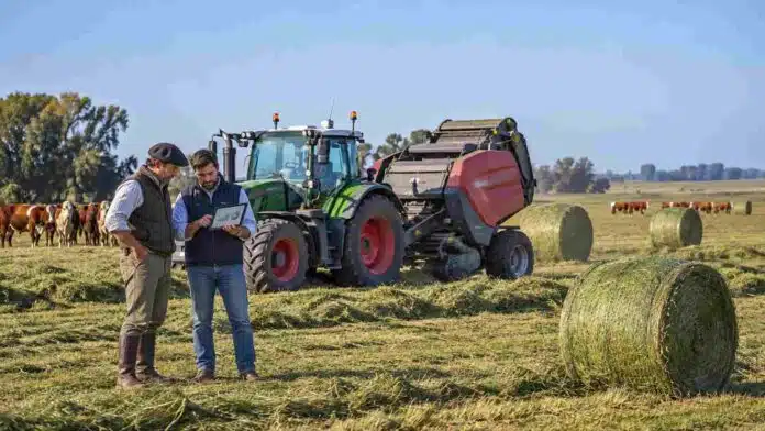 Productor y asesor técnico analizan datos en una tablet junto a un tractor Fendt 700 Vario con rotoenfardadora Massey Ferguson, rollos de alfalfa y rodeo Hereford en un campo argentino.