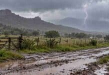 Alerta por lluvias persistentes en Córdoba, La Rioja y San Luis: dónde podrían superar los 40 mm Lluvias intensas sobre un paisaje rural serrano, con camino de tierra inundado, charcos y un relámpago bajo nubes de tormenta.