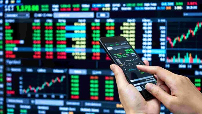mercado-financiero-cotizaciones-bolsa-ruralnet Persona operando desde un teléfono móvil frente a pantallas con cotizaciones y gráficos del mercado financiero.