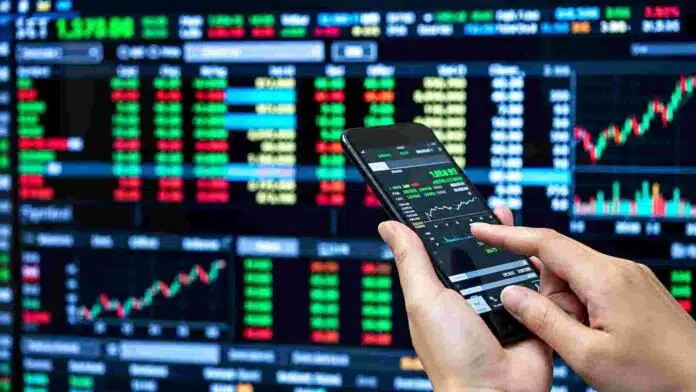 mercado-financiero-cotizaciones-bolsa-ruralnet Persona operando desde un teléfono móvil frente a pantallas con cotizaciones y gráficos del mercado financiero.