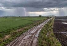 Pronóstico del 15 al 17 de octubre: lluvias y tiempo inestable en Buenos Aires, Córdoba y el Litoral Vista aérea de campos agrícolas y camino rural embarrado, con lluvias y un relámpago bajo un cielo de tormenta en la región pampeana argentina.